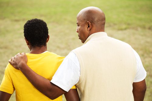 Talk with your teen, African American dad with arm around teenage son - view from behind them - teen