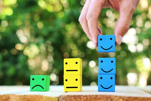 hand stacking colored blocks with frowning or smiling faces on them - affirmations - COVID-19