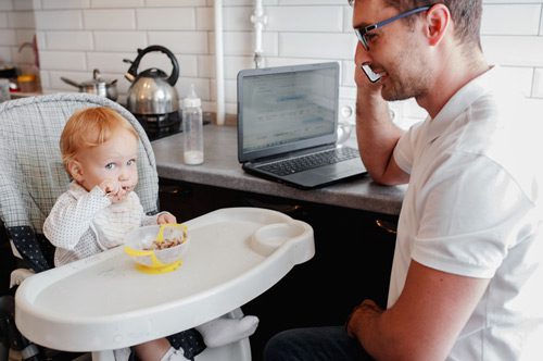 father on cell phone at home while feeding small child in high chair - spouse and rehab
