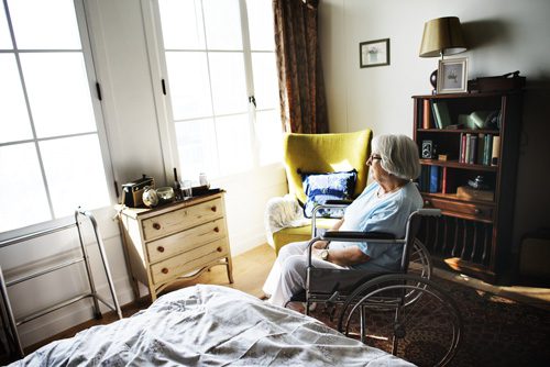 woman in her seventies in a wheelchair looking out a bedroom window - loneliness and addiction