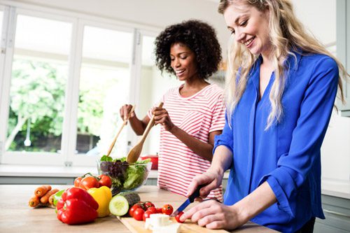 two beautiful young women making salad together at home - healthy eating